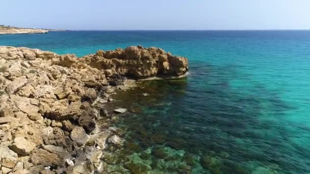 海蓝色的海水和岩石拍成的4k片断，平静的大海冲刷着岩石山，世界的边缘和蓝色的海滩，戏剧性的地质奇迹，美丽的风景 — 图库视频影像