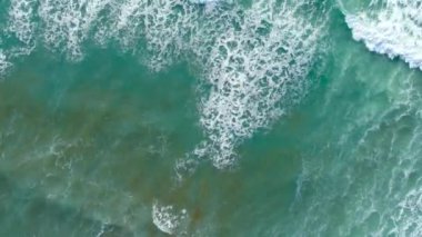 Okyanus dalgaları yukarıdan geliyor. Mavi turkuaz okyanusta 4K drone görüntüsü, dalga kırma, badana. Deniz üzerinde güneşli bir gün. Büyük dalgalar sahil şeridini vurdu. Güçlü dalgalar