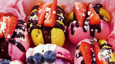Makarna, el yapımı güzel tatlı yiyecekler, taze çilek ve çikolatayla süslenmiş yabanmersini, narin sarı ve pembe kekler, şeker ve sağlıklı yiyecekler.