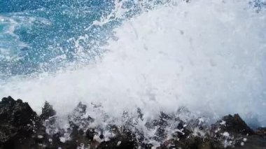 Deniz fırtınası konsepti, okyanus mavi su ve kayaların 4k manzara görüntüsü, güneşli gündüz deniz manzarası, yıkıcı ve muhteşem, okyanus dalgaları kıyıdaki kayalara çarpıyor ve bir su patlaması yaratıyor.