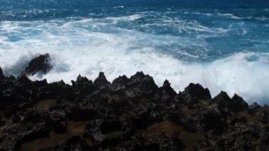 Tehlikeli kayaların üzerinden geçen dalgalar, Deniz fırtınası konsepti, güneşli deniz manzarası, yıkıcı ve muhteşem, okyanus dalgaları kıyıdaki kayalara çarpıyor ve bir su patlaması yaratıyor, 4k