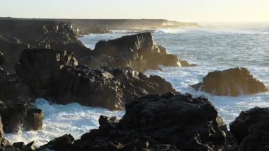 Atlantik Okyanusu kıyıları rüzgarlı havada, büyük dalgalar keskin siyah bazalt kayalara vuruyor, gün batımında İzlanda kıyıları, açık denizlerde fırtına. Yüksek kalite 4k görüntü