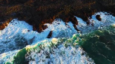 Atlantik Okyanusu kıyıları rüzgarlı havada, büyük dalgalar keskin siyah bazalt kayalara vuruyor, gün batımında İzlanda kıyıları, açık denizlerde fırtına. Yüksek kalite 4k görüntü