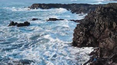 Atlantik Okyanusu kıyıları rüzgarlı havada, büyük dalgalar keskin siyah bazalt kayalara vuruyor, gün batımında İzlanda kıyıları, açık denizlerde fırtına. Yüksek kalite 4k görüntü