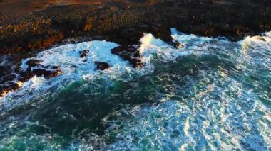 Atlantik Okyanusu kıyıları rüzgarlı havada, büyük dalgalar keskin siyah bazalt kayalara vuruyor, gün batımında İzlanda kıyıları, açık denizlerde fırtına. Yüksek kalite 4k görüntü