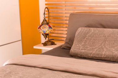 Oryantal lamba ahşap komodinin üzerinde, yatağın yanında, ahşap yatak başlığıyla.