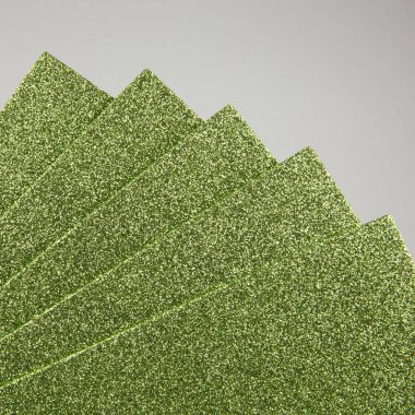 Yakından, arka planda köşegen şeklinde dizilmiş yeşil köpüklü çarşafları görebilirsiniz. Bu dekoratif materyalin parlak dokusu el işi projeler, ev yapımı el sanatları, tatil dekorasyonları, tasarımcı geçmişleri ve yaratıcı kavramlar için kullanılır..