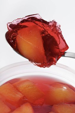 Meyve jölesinin sulu şeftali parçalarıyla yakın çekimi. Şeffaf doku ve zengin kırmızı ve turuncu renkler, tatlılar, tatlılar, yemek pişirme, restoran menüleri ve gıda reklamları için ideal bir görünüm yaratıyor..