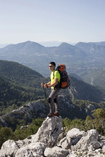 Νεαρός με σακίδιο στην κορυφή του βουνού μια ηλιόλουστη μέρα. — Φωτογραφία Αρχείου