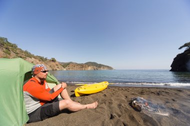 Adam kayak ve güneşli bir çadır ile sahilde.