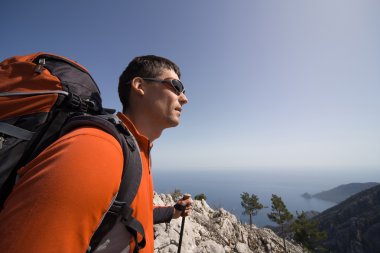 Güneşli bir günde bir dağın tepesinde sırt çantalı genç bir adam.