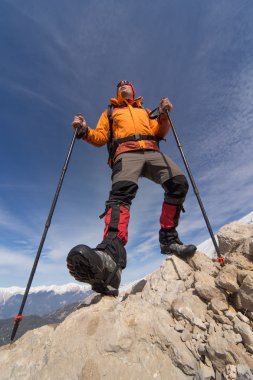Güneşli bir günde bir karla kaplı dağın tepesinde sırt çantası ile genç adam.