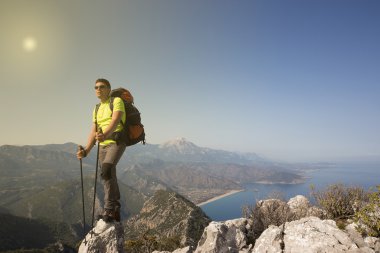 Güneşli bir günde bir dağın tepesinde sırt çantalı genç bir adam.