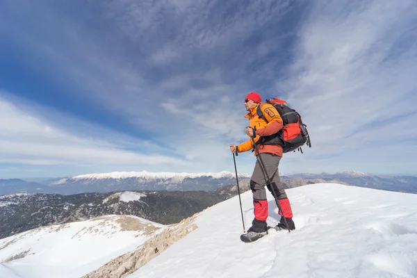 O jovem com a mochila no topo de uma montanha coberta de neve em um dia ensolarado . — Fotografia de Stock