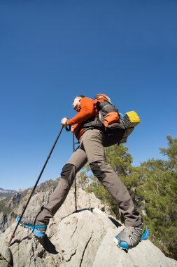 Güneşli bir günde bir dağın tepesinde sırt çantalı genç bir adam.