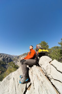 Güneşli bir günde bir dağın tepesinde sırt çantalı genç bir adam.