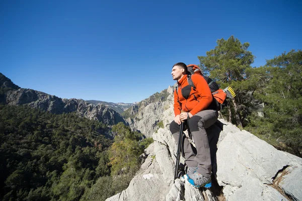 Güneşli bir günde bir dağın tepesinde sırt çantalı genç bir adam. — Stok fotoğraf