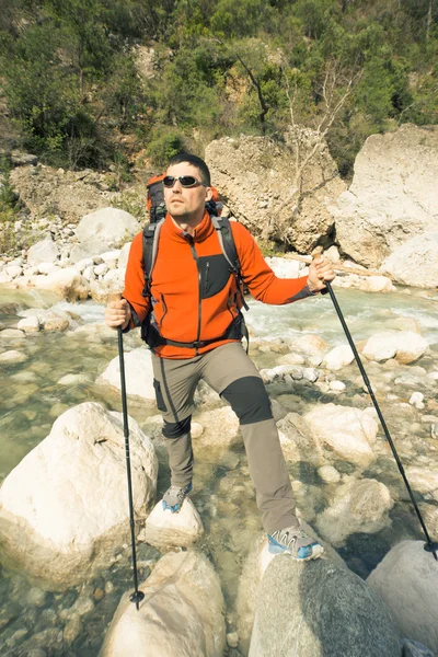 Joven con una mochila para mover un río de montaña en un día soleado . — Foto de Stock