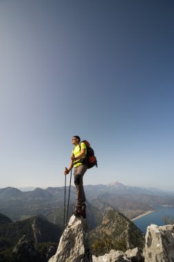 Güneşli bir günde bir dağın tepesinde sırt çantalı genç bir adam.