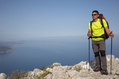 Güneşli bir günde bir dağın tepesinde sırt çantalı genç bir adam.