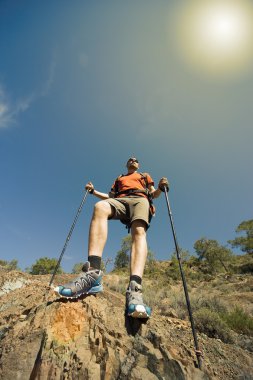 Güneşli bir günde bir dağın tepesinde sırt çantalı genç bir adam.