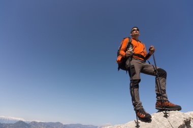 Güneşli bir günde bir dağın tepesinde sırt çantalı genç bir adam.