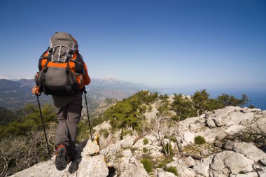 Güneşli bir günde bir dağın tepesinde sırt çantalı genç bir adam.
