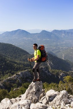 Güneşli bir günde bir dağın tepesinde sırt çantalı genç bir adam.