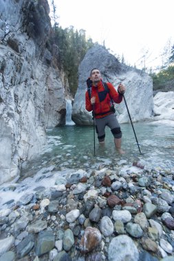 Genç adam bir sırt çantası ile bir dağ nehir taşımak için.