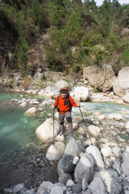 Genç adam bir sırt çantası ile bir dağ nehir taşımak için.