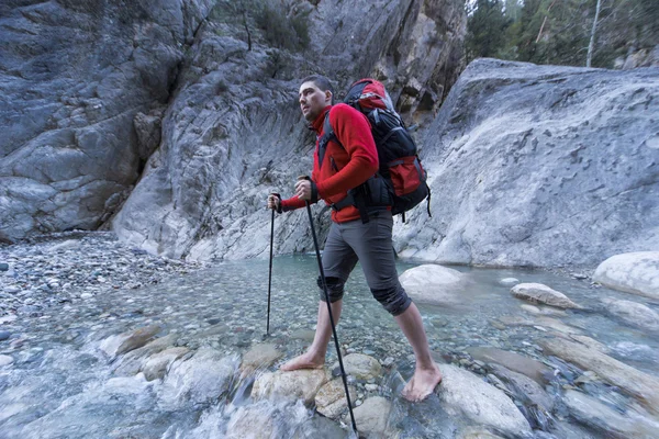 Joven con una mochila para mover un río de montaña . — Foto de Stock