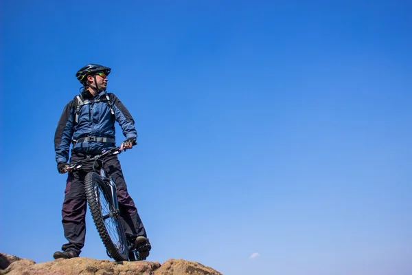 El tipo en la cima de la montaña con la bicicleta. contra el cielo azul . — Foto de Stock