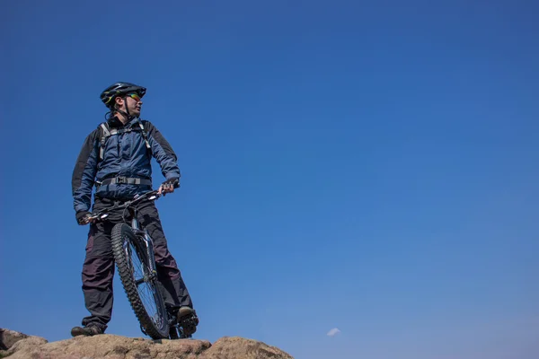 El tipo en la cima de la montaña con la bicicleta contra el cielo azul . — Foto de Stock