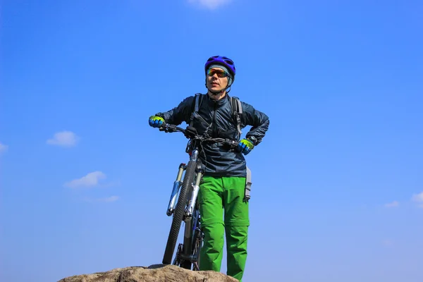 El tipo en la cima de la montaña con la bicicleta contra el cielo azul . — Foto de Stock