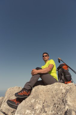 Güneşli bir günde bir dağın tepesinde sırt çantalı genç bir adam. 