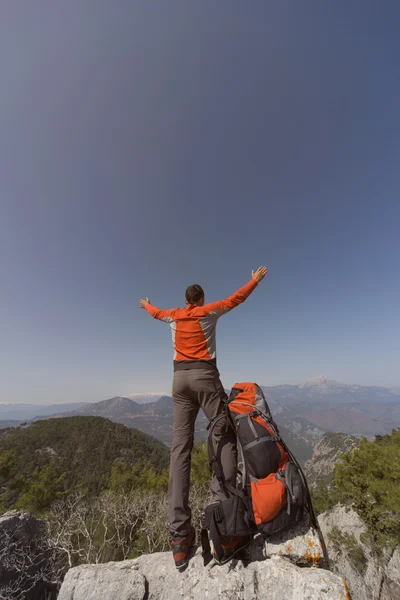 Mladý muž s batohem na vrcholu hory za slunečného dne. — Stock fotografie