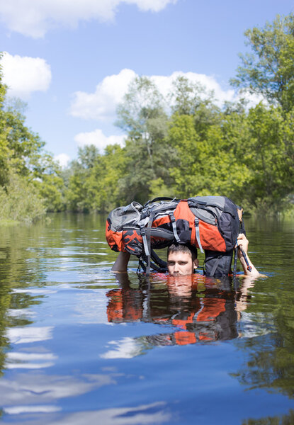 Человек, переходящий реку с рюкзаком
.