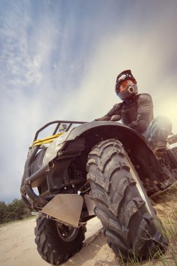 A man riding ATV in sand in protective clothing and a helmet. clipart