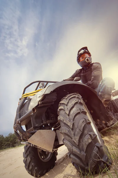 Um homem montando ATV na areia em roupas protetoras e um capacete . — Fotografia de Stock