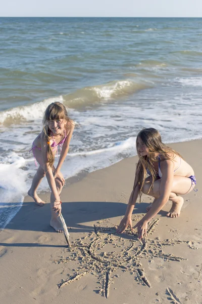 Chicas dibujando en la arena en la playa en el sol de verano . —  Fotos de Stock