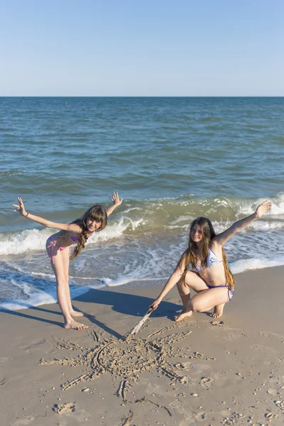 女孩在夏日的阳光下的海滩上在沙画. — 图库照片