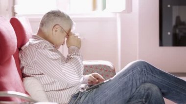 sevimli ihtiyar evde tablet bilgisayar kullanarak kırmızı koltukta oturan