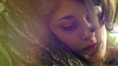Parkta hayal kuran üzgün, güzel bir kadının kucaklaşma ağacının 4K görüntüsü.