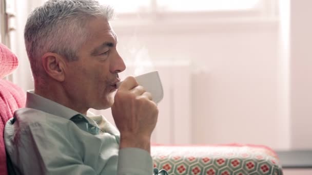 Leuke man drinken koffie zittend op de rode sofa in de woonkamer — Stockvideo