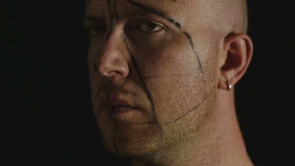 Giovane uomo con segni neri sul viso nelle tenebre — Video Stock