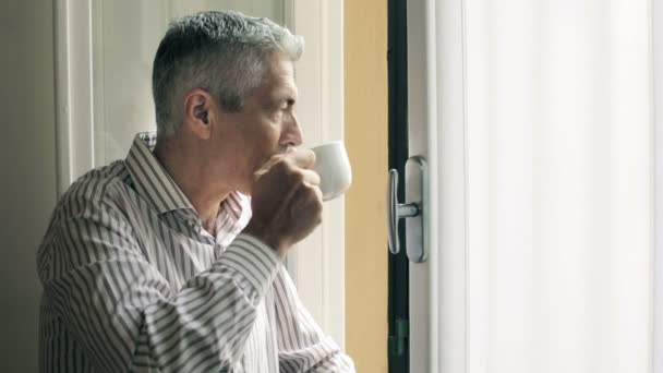 Homem pensativo bebendo chá quente na janela: café, bebida, vapor, olhar — Vídeo de Stock