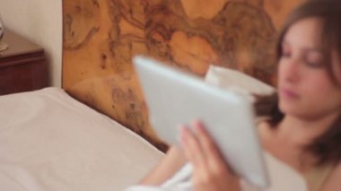Yatağa kullanarak ve dijital tablet tutan genç güzel kadın