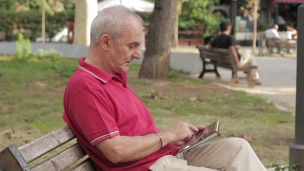 Senior man met behulp van tablet pc in park — Stockvideo