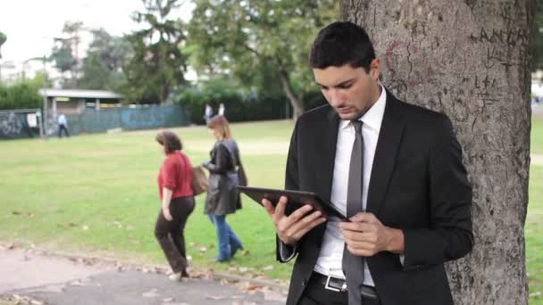 Giovane uomo d'affari sotto l'albero utilizzando tablet — Video Stock