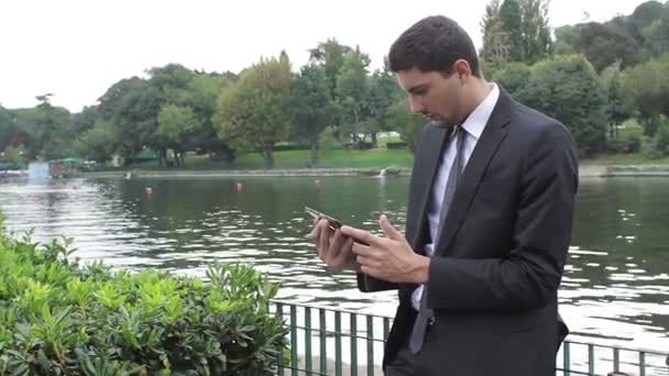 Jovem empresário usando tablet pc perto de um lago — Vídeo de Stock